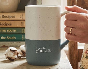 May include: A two-toned ceramic mug with a speckled finish, featuring a white upper section and a dark blue lower section. The name Katie is printed in white script on the blue portion, accompanied by a small heart icon next to the name.