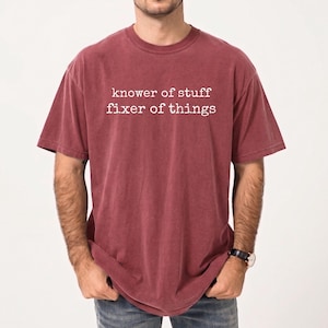 Op de afbeelding: Bordeauxrood T-shirt met de witte tekst "knower of stuff fixer of things". Het shirt met korte mouwen heeft een ronde hals en een licht vervaagde uitstraling. De stof voelt zacht aan.