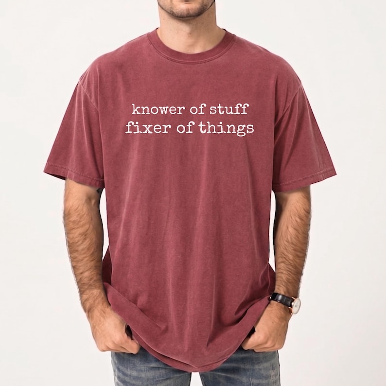 Op de afbeelding: Bordeauxrood T-shirt met de witte tekst "knower of stuff fixer of things". Het shirt met korte mouwen heeft een ronde hals en een licht vervaagde uitstraling. De stof voelt zacht aan.