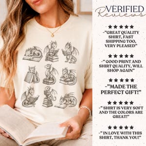 K&ouml;nnte beinhalten: Ein cremefarbenes T-Shirt mit einem Grafikdruck von neun kleinen Drachen, die in verschiedenen Posen mit B&uuml;chern interagieren. Der Text auf der rechten Seite zeigt verifizierte F&uuml;nf-Sterne-Bewertungen mit Kundenkommentaren zur Qualit&auml;t.