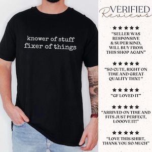 Op de afbeelding: Zwart t-shirt met de tekst "knower of stuff fixer of things" in het wit. Het shirt heeft een ronde hals. De afbeelding bevat ook klantbeoordelingen.