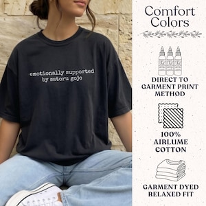 May include: A black short-sleeve t-shirt with the white text "emotionally supported by satoru gojo" printed on the chest. The shirt features a relaxed fit and is made of 100% airlume cotton, utilising a direct to garment print method.