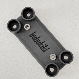 May include: A black plastic phone mount with the word "bubulki" printed on it. The mount has four holes for screws and two small metal inserts.