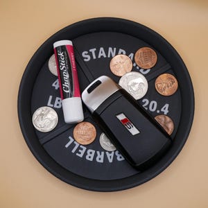 May include: A black tray with the words "STANDARD BARBELL 20.4" printed on it. There are several US coins and a black car key with a red and white logo. A tube of ChapStick lip balm is also on the tray.