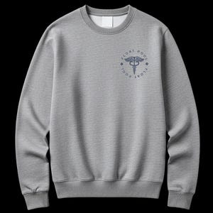 May include: A heather gray crewneck sweatshirt featuring a dark blue circular graphic on the upper left chest. The design includes a caduceus symbol in the center, surrounded by the text FLOAT POOL and two small cross icons on the sides.