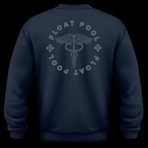May include: A navy blue long-sleeve sweatshirt featuring a circular graphic on the back. The design includes a central caduceus symbol, the text FLOAT POOL repeated in a circle, and two small plus signs on the left and right sides of the circle.