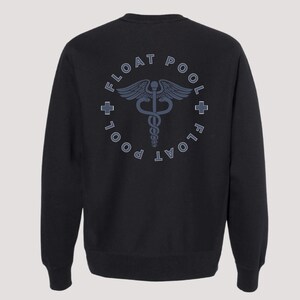 May include: A black long-sleeve sweatshirt featuring a circular graphic on the back. The design includes the text FLOAT POOL in a circular arrangement, two small cross symbols, and a central caduceus emblem in a muted blue-gray color.
