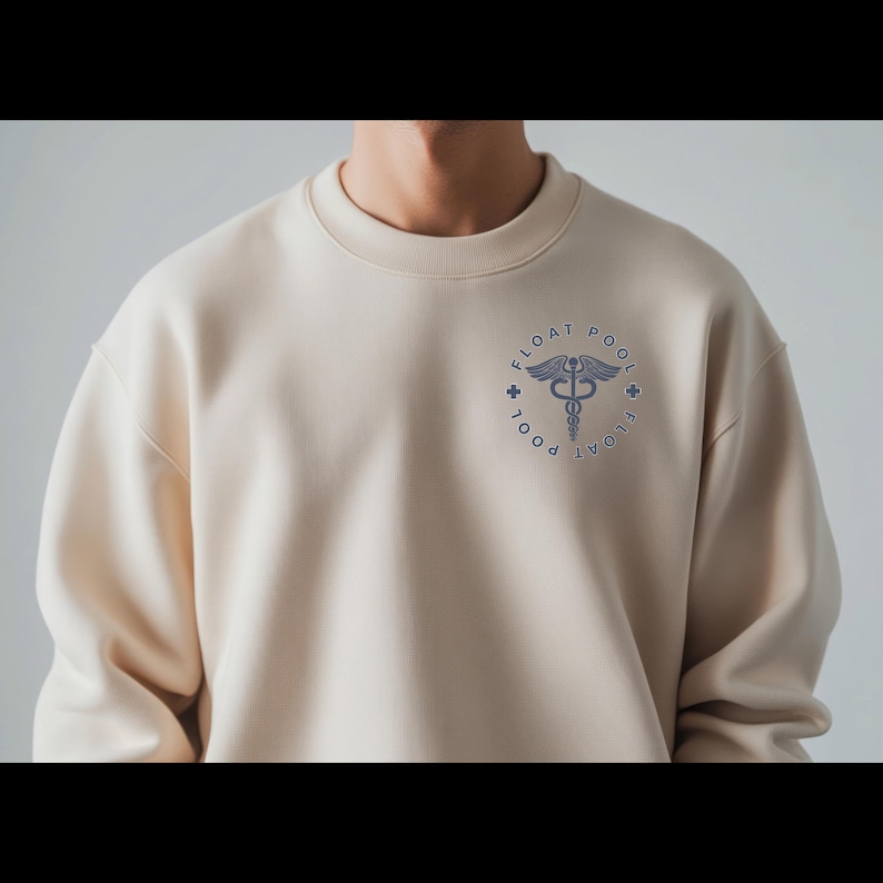 May include: A beige crewneck sweatshirt featuring a circular navy blue graphic on the left chest. The design includes a caduceus symbol in the center, surrounded by the text "FLOAT POOL" and two small cross icons on the left and right sides.