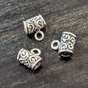 May include: Three silver-toned metal end caps with a decorative swirl design. Each end cap has a small loop for attaching to a cord or chain.