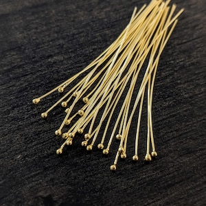 May include: A bunch of gold head pins with round heads. The pins are arranged in a fan shape on a dark wooden surface.