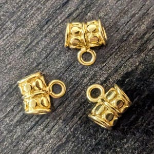 May include: Three gold-toned metal cord end caps with a decorative design. Each cap has a small loop at the top.
