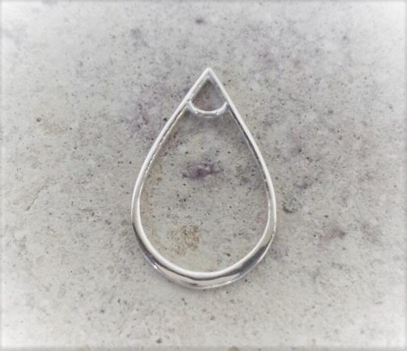 May include: A silver-colored, teardrop-shaped pendant with a small triangle at the top. The pendant is set against a textured, gray background. The design is simple and elegant.