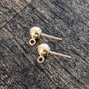 May include: Two gold-toned earring posts with a round ball at the top and a loop at the bottom.
