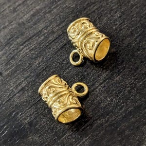 May include: Two gold-tone metal cord end caps with an ornate design. Each cap has a small loop at the top.
