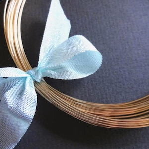 May include: A bundle of gold-colored wire tied with a light blue ribbon. The wire is arranged in a circular shape.