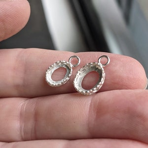 May include: Two silver oval-shaped pendant settings with a textured edge and a jump ring.