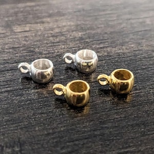 May include: Four small metal cup-shaped charms with a loop for attaching to jewelry. Two charms are gold, and two are silver.