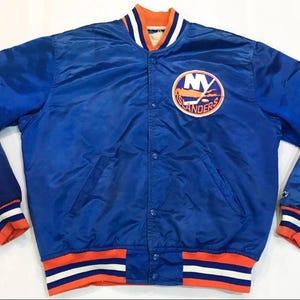 May include: A blue satin jacket with the NY Islanders logo on the chest. The jacket has orange, white, and blue striped cuffs and waistband. The collar is orange and white.