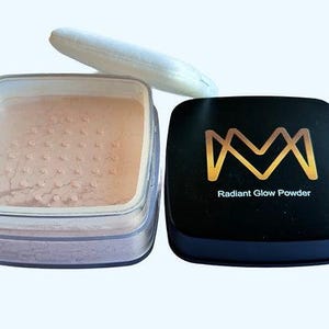 K&ouml;nnte beinhalten: Ein quadratischer, klarer Beh&auml;lter gef&uuml;llt mit pfirsichfarbenem Puder, ein wei&szlig;es Puderquaste und ein schwarzes Kompaktpuder mit goldfarbenem Schriftzug "Radiant Glow Powder". Das Make-up befindet sich auf einem hellen Hintergrund.