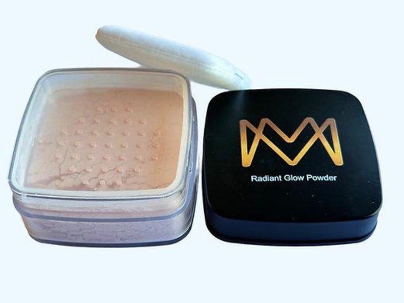K&ouml;nnte beinhalten: Ein quadratischer, klarer Beh&auml;lter gef&uuml;llt mit pfirsichfarbenem Puder, ein wei&szlig;es Puderquaste und ein schwarzes Kompaktpuder mit goldfarbenem Schriftzug "Radiant Glow Powder". Das Make-up befindet sich auf einem hellen Hintergrund.