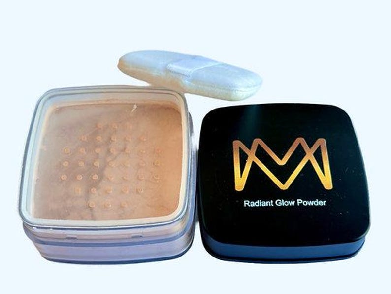 K&ouml;nnte beinhalten: Offener Kompaktpuder von Radiant Glow Powder mit hellem Beige, einem wei&szlig;en Puderquaste und einem schwarzen Kompaktdosendeckel mit goldenem "M"-Logo und den Worten "Radiant Glow Powder". Der Kompaktpuder ist ge&ouml;ffnet und zeigt das Puder.