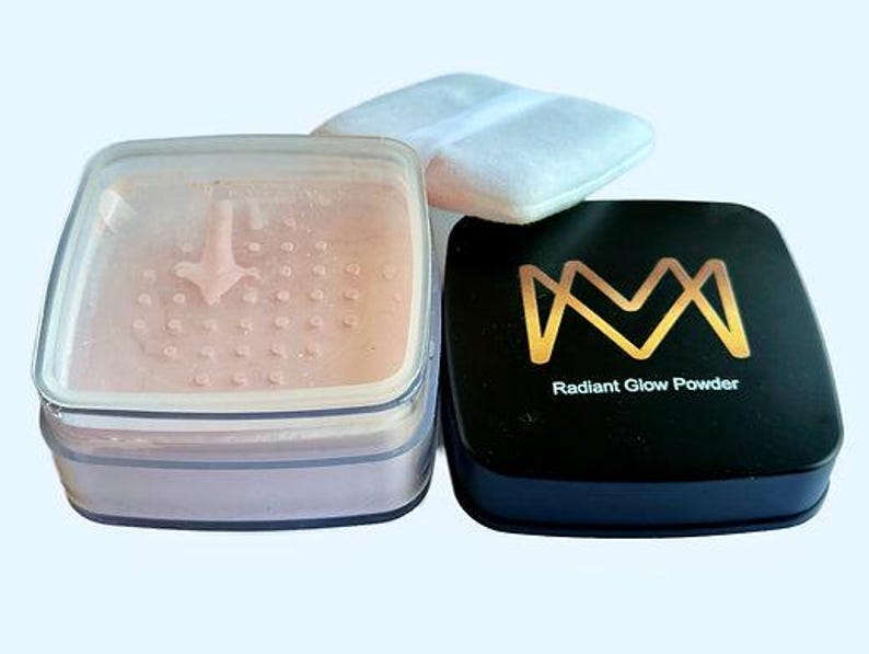 K&ouml;nnte beinhalten: Ein Set von Make-up-Produkten, darunter ein durchscheinender Puder-Kompakt, ein schwarzer Kompakt mit goldfarbenem Schriftzug "Radiant Glow Powder" und ein wei&szlig;es Puderquaste. Das transparente Puder befindet sich in einem transparenten, quadratischen Beh&auml;lter.