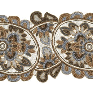 May include: A beaded table runner with a paisley design. The runner features a cream-coloured background with brown, grey, and gold floral and paisley patterns. The edges are outlined with small beads.