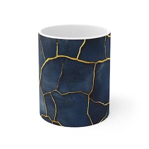 Może przedstawiać: Biały kubek ceramiczny z niebieskim i złotym wzorem. Wzór przedstawia pęknięty wzór ze złotymi liniami.