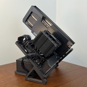 Op de afbeelding: Een zwart computeronderdeel met een koelventilator en een zwarte standaard. Het onderdeel is schuin op de standaard gemonteerd.