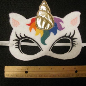 May include: White felt unicorn mask with a rainbow mane and a gold horn. The mask has black eyelashes and a white elastic band.