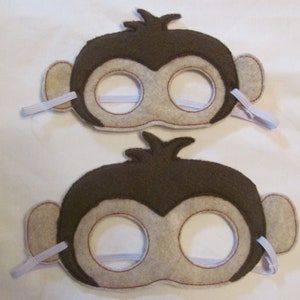May include: Two brown felt monkey masks with white elastic straps. The masks have brown felt ears and brown felt hair.