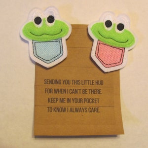 May include: Two felt frog pocket hug patches with a message on a brown card that reads: "Sending you this little hug for when I can't be there. Keep me in your pocket to know I always care."