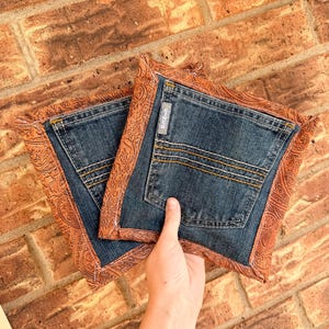 Pode incluir: Duas pegas quadradas feitas de tecido de ganga azul com um bolso traseiro com a palavra CINCH numa pequena etiqueta. A ganga é contornada por um rebordo de tecido castanho com um padrão paisley em relevo e costuras visíveis.