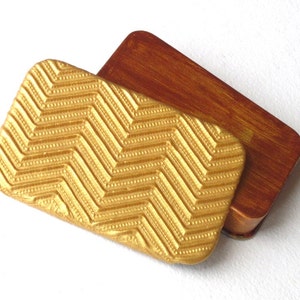 May include: A small, rectangular box with a gold lid featuring a chevron pattern. The box is made of wood and has a brown finish.