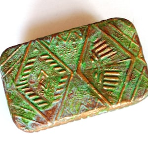 May include: A rectangular copper box with a green patina and a geometric design. The box has a textured surface and a raised design.