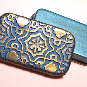 May include: Two teal blue metal boxes with a decorative gold pattern on one box. The boxes are rectangular and have a slightly rounded edge.