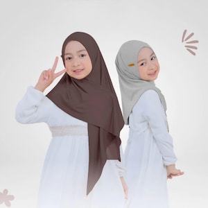 May include: Two hijabs, one in dark brown and one in light grey, worn over white long-sleeved dresses. The dark brown hijab is draped over the head and shoulders, while the light grey hijab features a small gold-coloured accent on the side.
