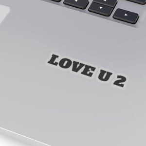 May include: A silver laptop featuring a black keyboard and the text "LOVE U 2" in black lettering on the lower right corner of the laptop.