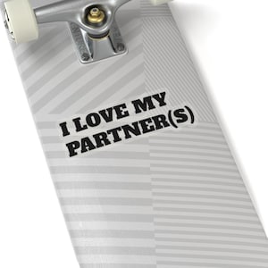 May include: A white sticker with the text "I LOVE MY PARTNER(S)" in black, placed on a skateboard deck. The deck has a gray and white striped pattern. The skateboard's metal truck and wheels are visible.