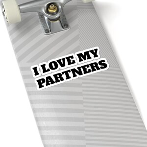 May include: A white sticker with the text "I LOVE MY PARTNERS" in bold black letters. The sticker is on a skateboard deck with a grey and white striped pattern. The skateboard's metal truck and wheels are visible.