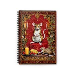 May include: A spiral bound notebook with a colorful illustration of a mouse sitting on a throne with a plate of cheese and cherries. The mouse is surrounded by candles and floral designs.