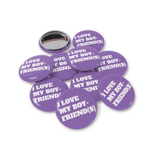 Op de afbeelding: Een verzameling paarse ronde buttons met de witte tekst "I LOVE MY BOYFRIEND(S)". Eén button is apart en toont de speld. De buttons liggen op een witte achtergrond.