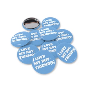 Peut inclure: Plusieurs badges ronds bleu clair avec l'inscription blanche "I LOVE MY BOYFRIEND(S)". Un badge montre l'arrière avec l'épingle. Les badges sont disposés sur un fond blanc.