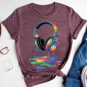 a purple t-shirt with a colorful graphic of a pair of headphones, along with a pair of jeans and a pair of glasses.