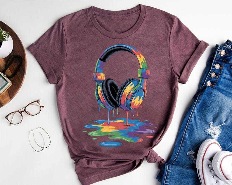 a purple t-shirt with a colorful graphic of a pair of headphones, along with a pair of jeans and a pair of glasses.