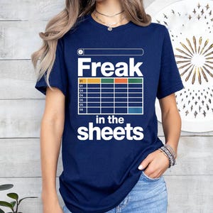 May include: Navy blue t-shirt with the text "Freak in the sheets" in white. The design includes a spreadsheet-like graphic with colored boxes. The shirt is a casual wear item.