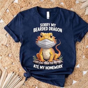 A navy blue t-shirt with a cartoon image of a bearded dragon and text that says "Sorry my bearded dragon ate my homework".