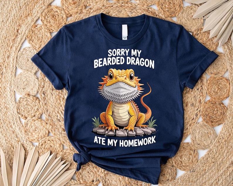 A navy blue t-shirt with a cartoon image of a bearded dragon and text that says "Sorry my bearded dragon ate my homework".