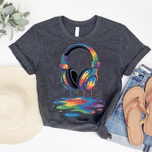 a gray t-shirt with a colorful graphic of a pair of headphones, along with a hat, jeans, and sandals, all laid out on a white background.