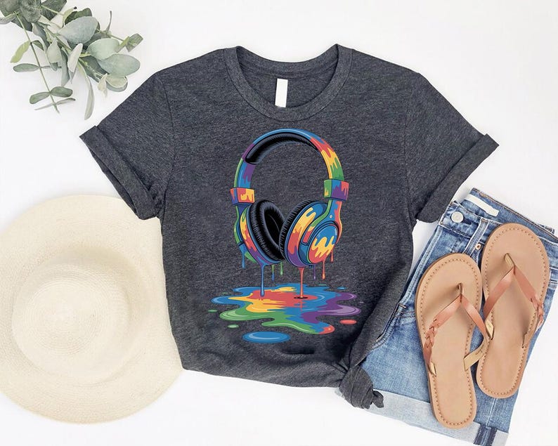 a gray t-shirt with a colorful graphic of a pair of headphones, along with a hat, jeans, and sandals, all laid out on a white background.